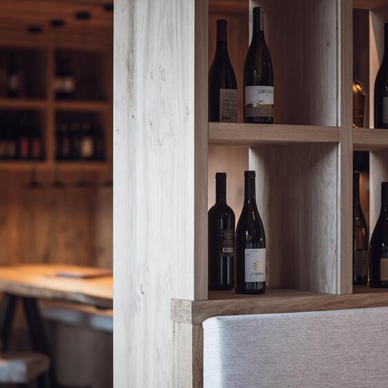 Open shelf with wine bottles, bar stools and a counter in the background.