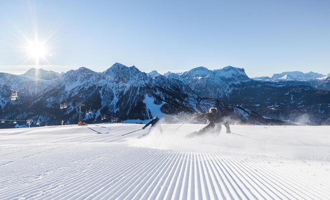 Skier on a freshly groomed ski slope with views of the snow-covered peaks of the Dolomites in the sunshine.