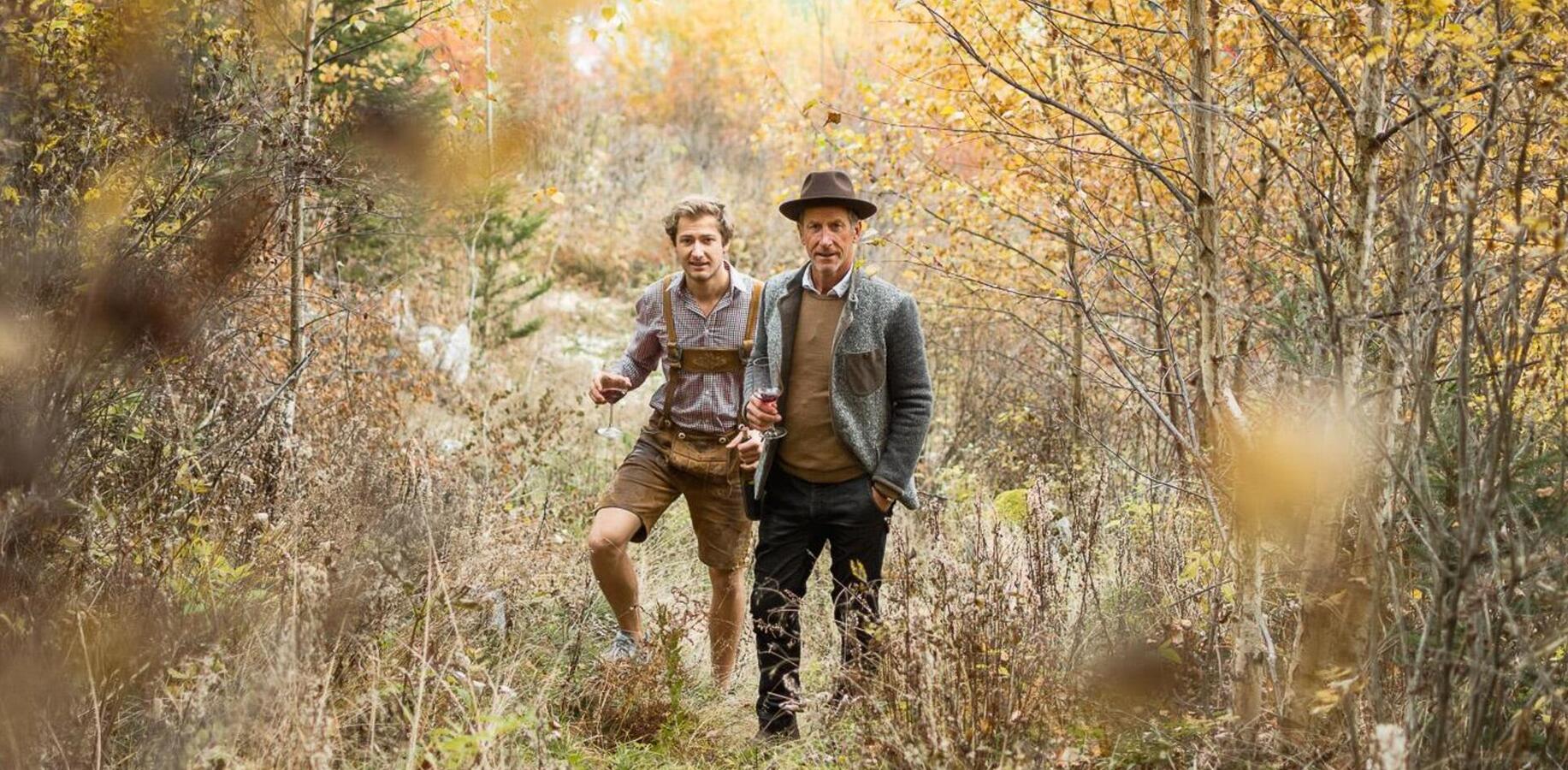 Two people with a glass of red wine in an autumn woodland.