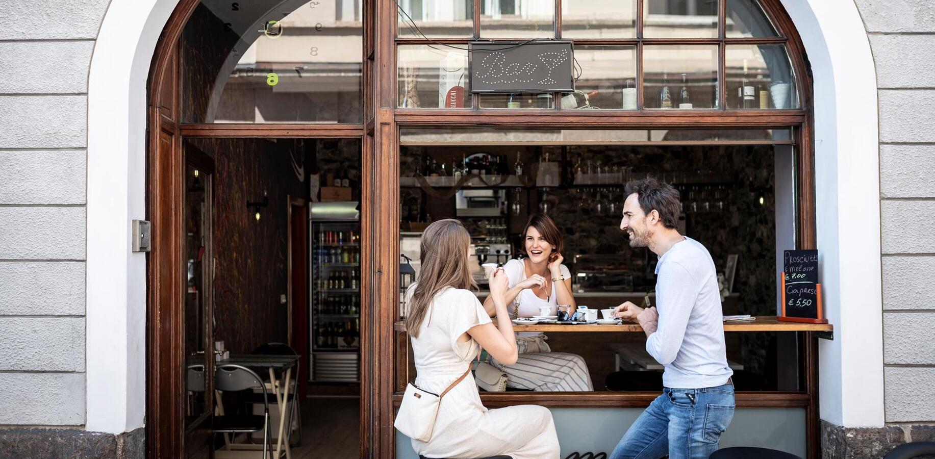 Three people enjoying coffee outdoors in front of a café.