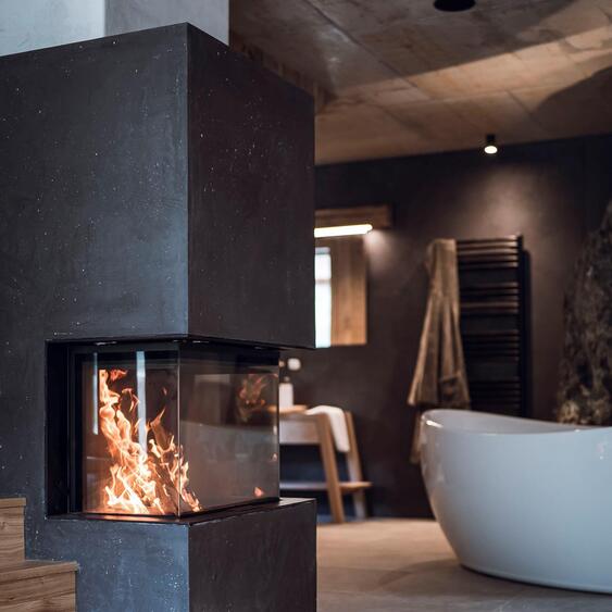 Freestanding bathtub beside a rock wall, with a lit fireplace in the foreground.