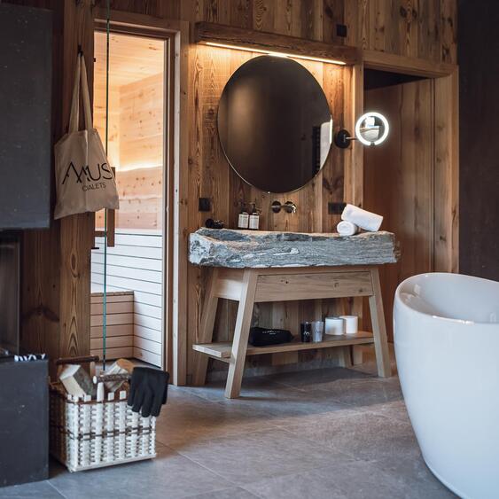 freistehende Badewanne vor einer Felswand, Natursteinwaschbecken und brennendem Kamin.
