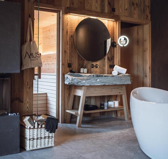 Vasca da bagno freestanding davanti a una parete rocciosa, lavabo in pietra naturale e camino acceso.