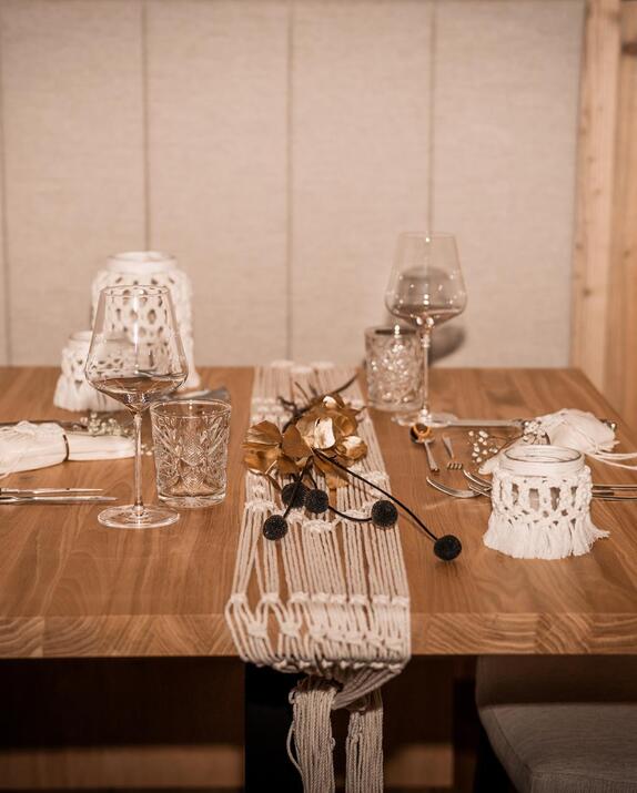 Set wooden table with wine glasses, white cloth napkins and macramé decorations inside the Amus Chalet.