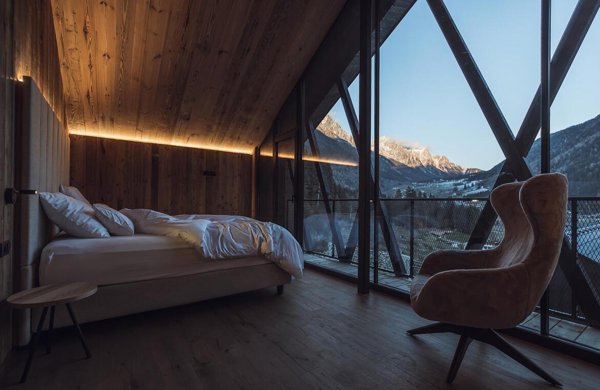 Chalet-Schlafzimmer mit Doppelbett, Holzwänden und großer Glasfront mit Blick auf verschneite Berge.