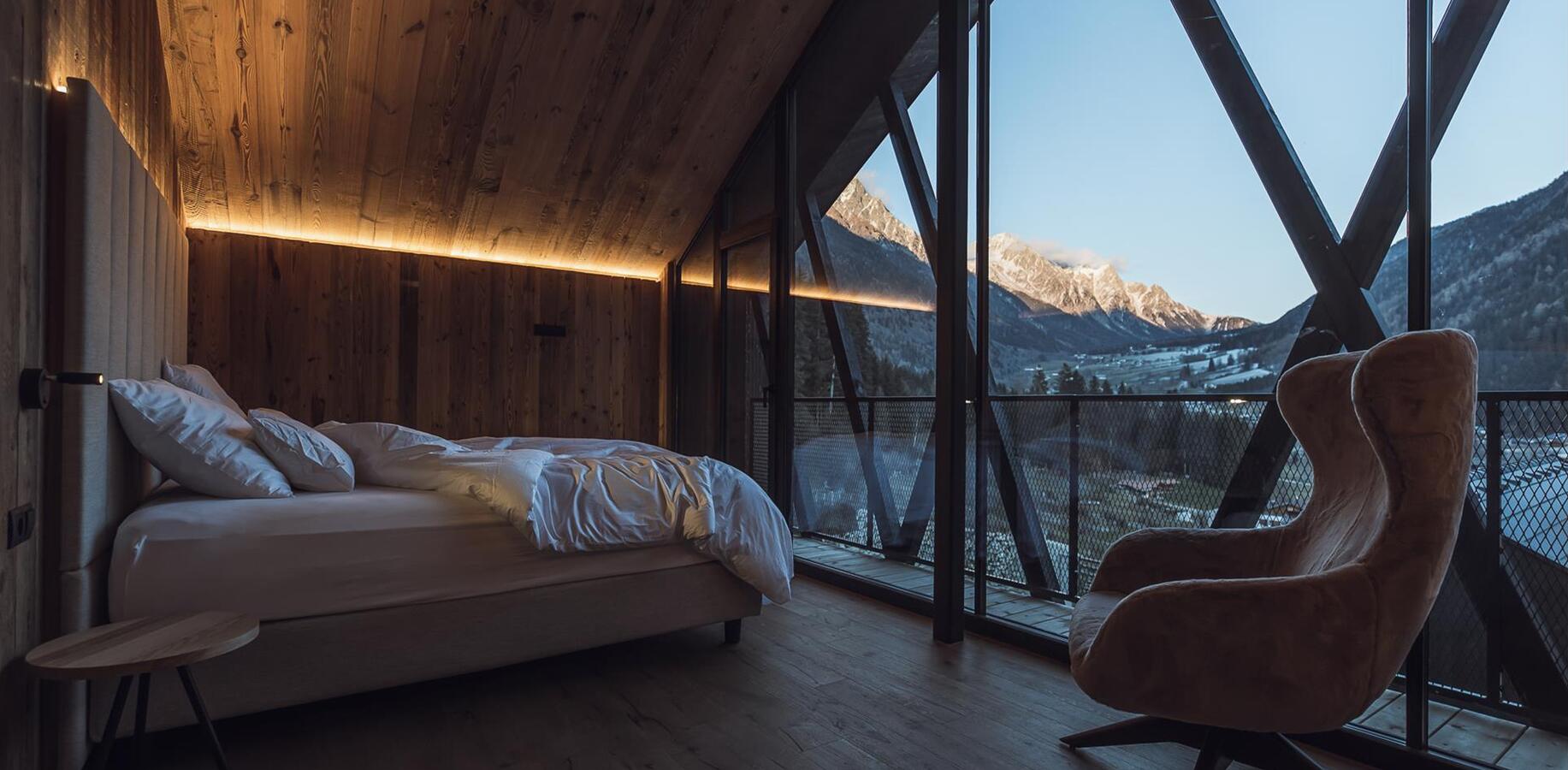 Chalet-Schlafzimmer mit Doppelbett, Holzwänden und großer Glasfront mit Blick auf verschneite Berge.