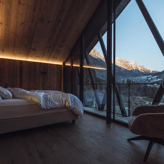 Camera da letto dello chalet con letto matrimoniale, pareti in legno e ampia vetrata con vista sulle montagne innevate.