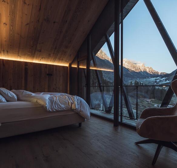 Camera da letto dello chalet con letto matrimoniale, pareti in legno e ampia vetrata con vista sulle montagne innevate.