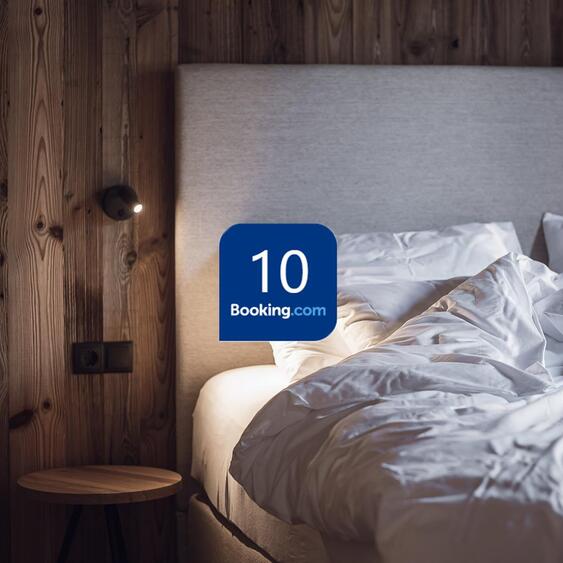 Doppelbett vor einer dunklen Holzwand und eingeblendetem Booking.com-Bewertungslogo mit der Note 10.