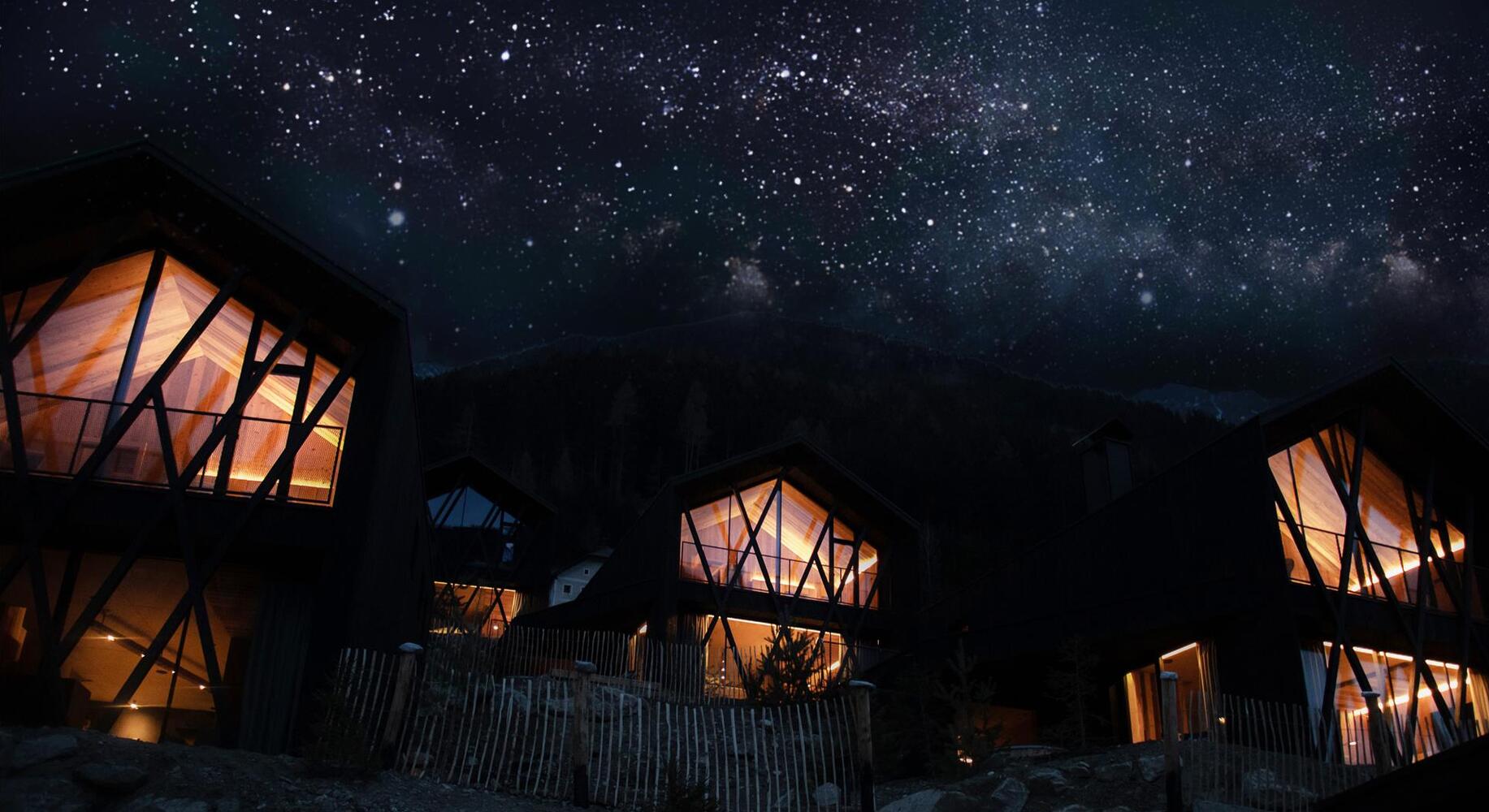Beleuchtete Amus Chalets mit großen Glasfronten unter einem funkelnden Sternenhimmel.