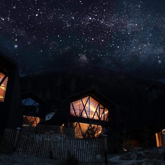 Beleuchtete Amus Chalets mit großen Glasfronten unter einem funkelnden Sternenhimmel.