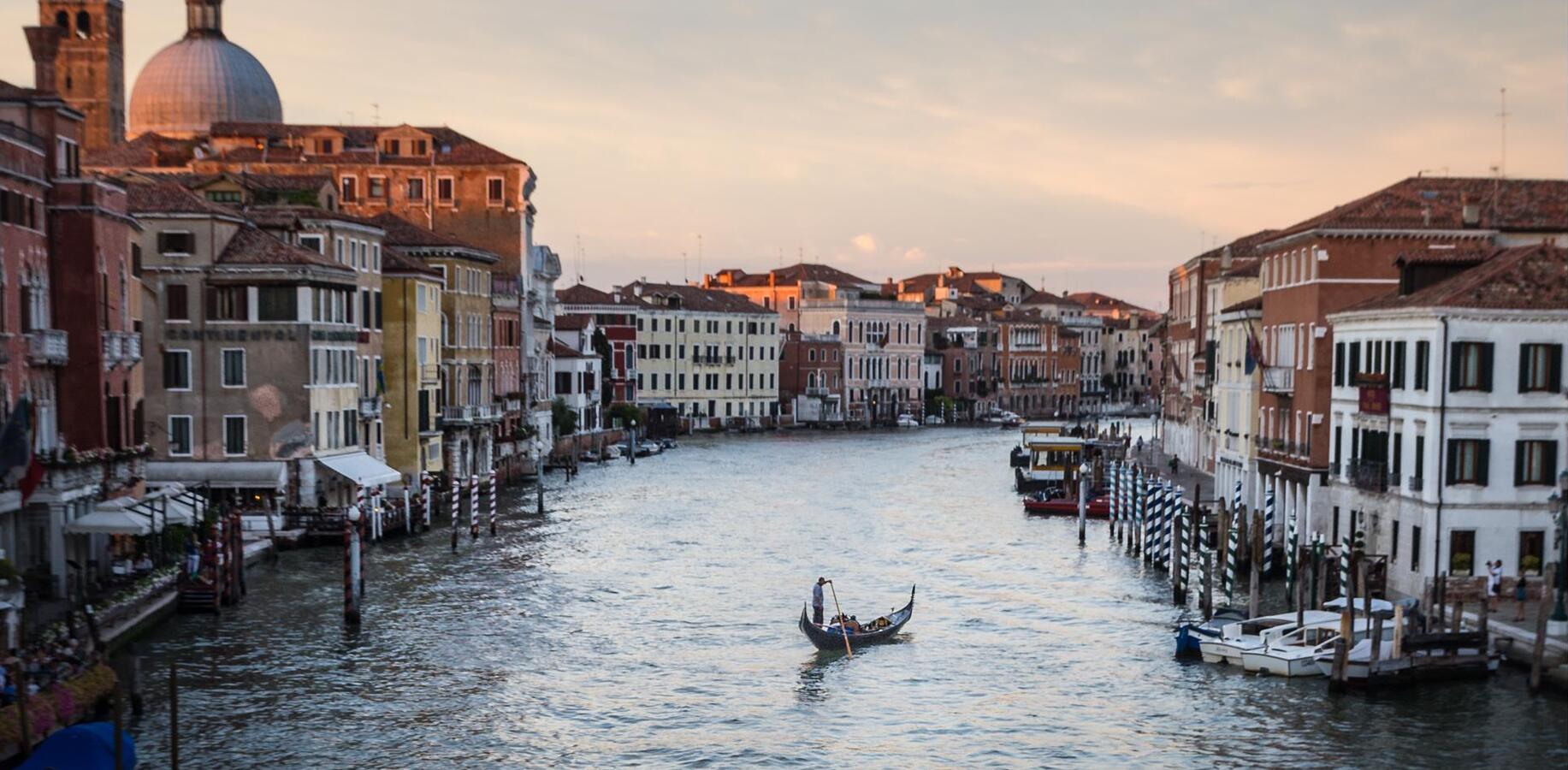 Blick auf einen Kanal in Venedig mit einer Gondel und historischen Gebäuden im warmen Licht des Sonnenuntergangs