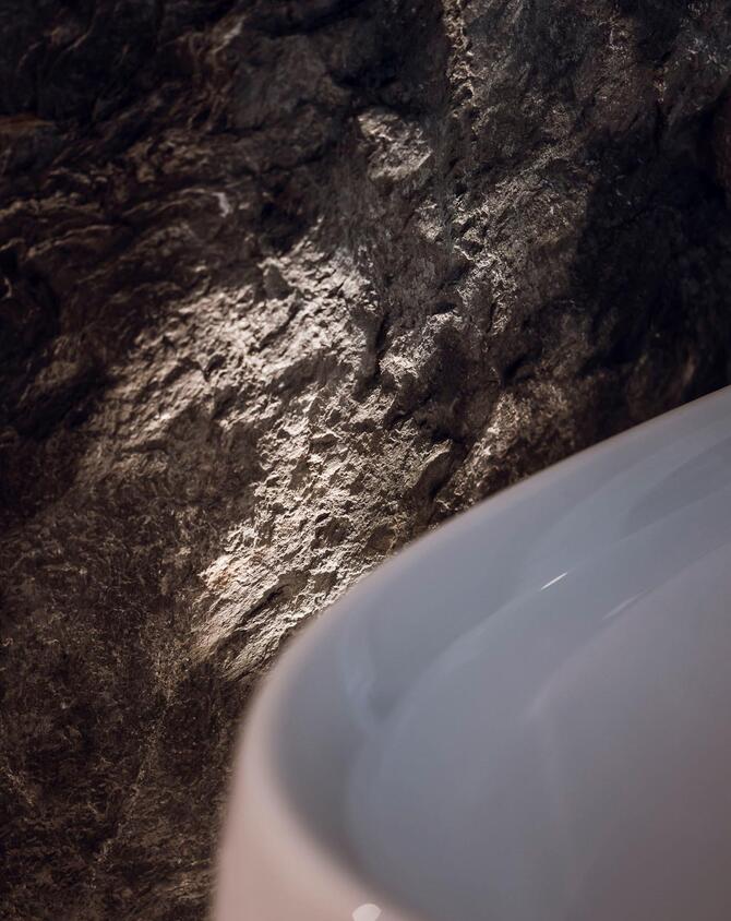 Detailansicht einer weißen Badewanne mit beleuchteter Felswand dahinter.