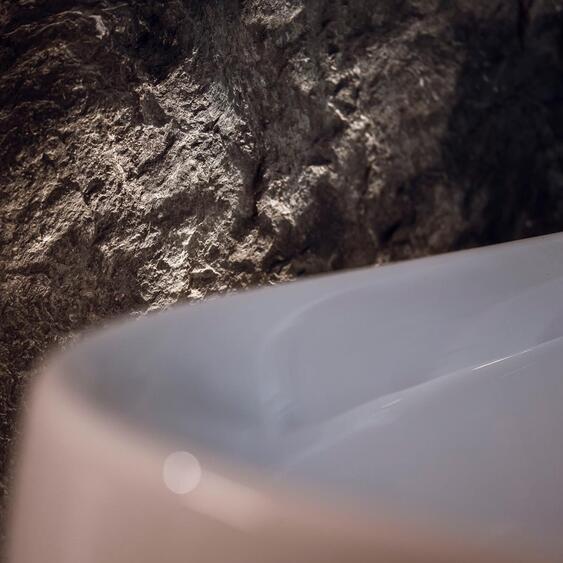 Detailansicht einer weißen Badewanne mit beleuchteter Felswand dahinter.