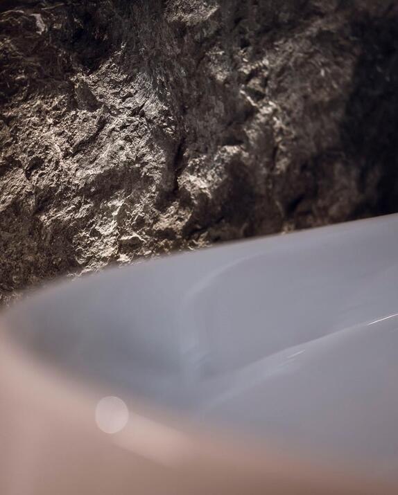 Detailansicht einer weißen Badewanne mit beleuchteter Felswand dahinter.