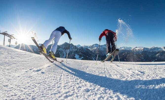 Zwei Skifahrer springen auf einer verschneiten Skipiste in die Luft.