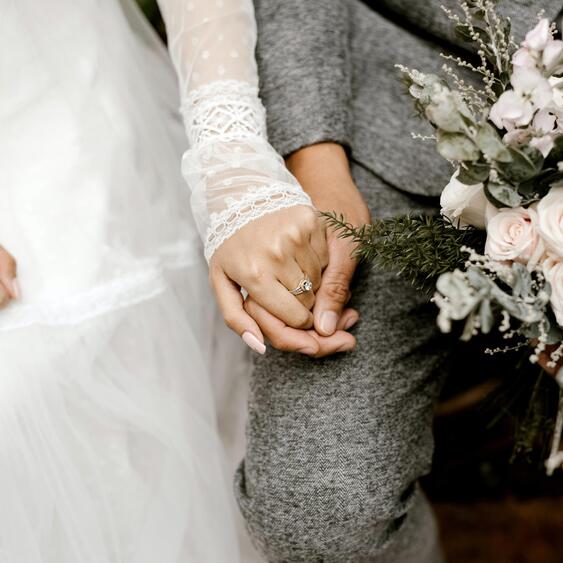 Coppia di sposi che si tiene per mano, con un bouquet di rose rosa chiaro.