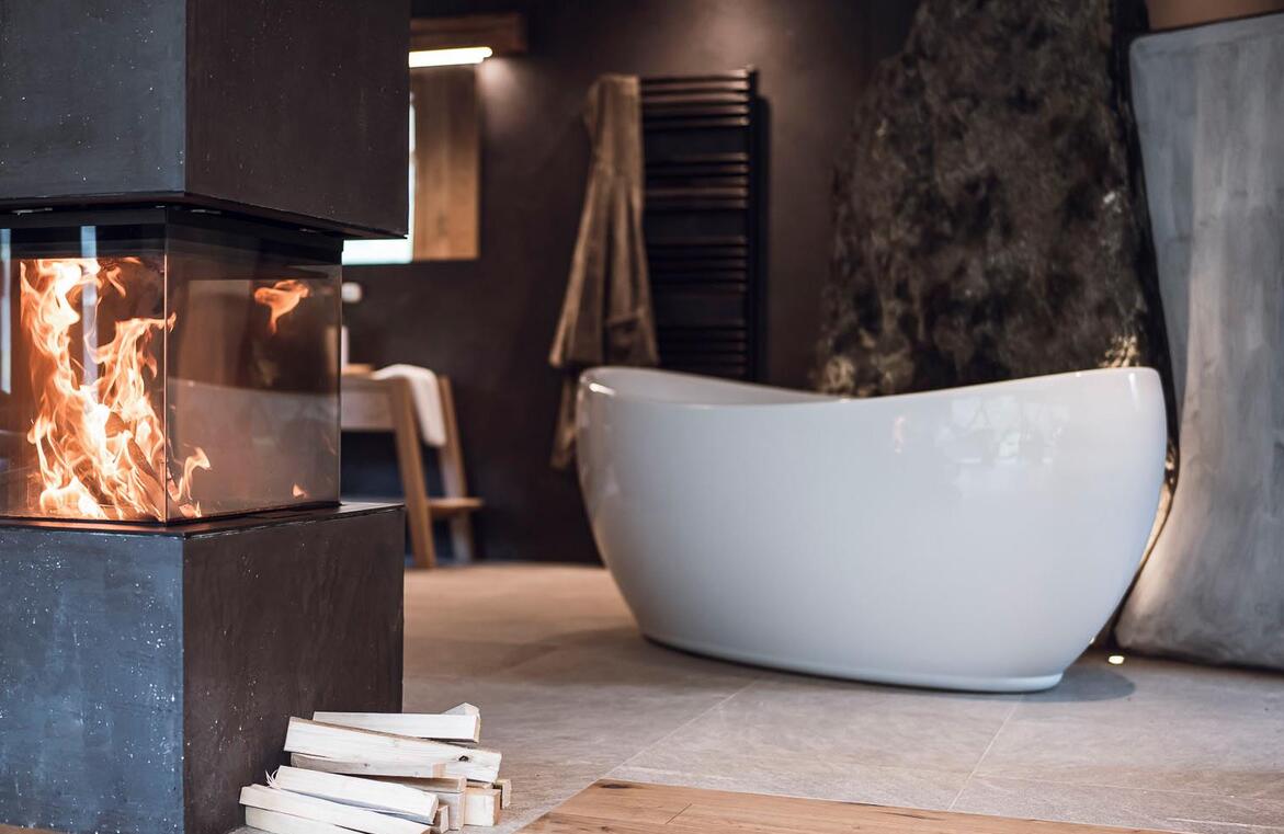 Freistehende Badewanne vor einer Felswand mit brennendem Kamin im Vordergrund.