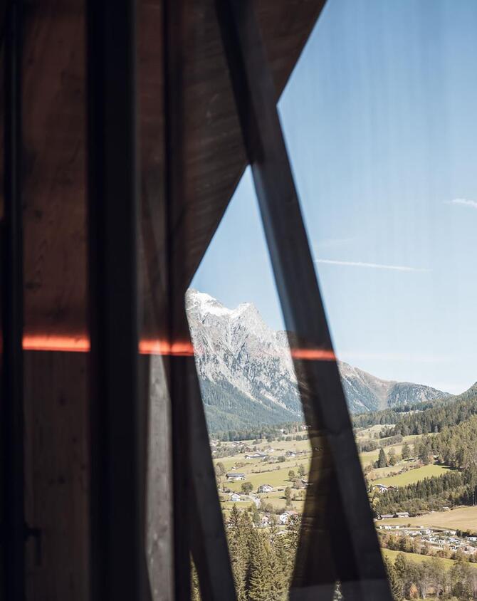 Blick vorbei an einem Amus Chalets auf ein grünes Tal, bewaldete Hänge und markante Berggipfel.