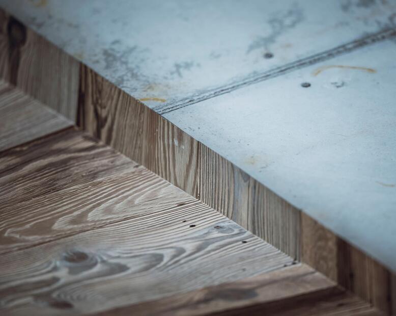 Detailansicht von Holz mit markanter Maserung am Übergang zu einer grauen Betonfläche.