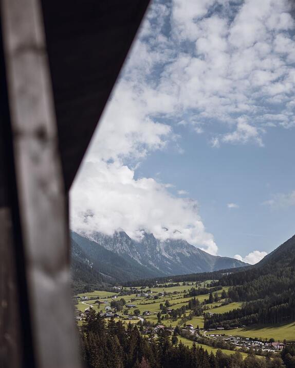 Blick auf Wiesen, Häuser, Wälder und Berge im Neben mit Chaletfassade im Vordergrund.