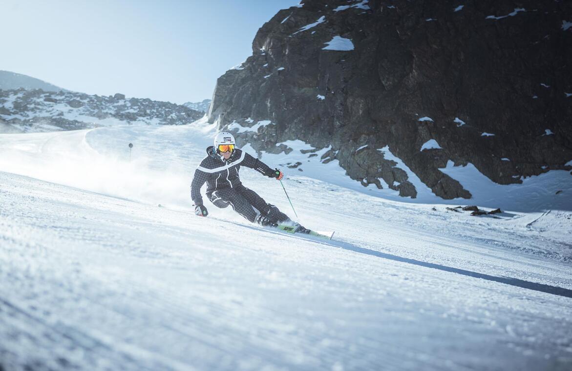 Sciatore su una pista da sci, con montagne e pareti rocciose sullo sfondo.