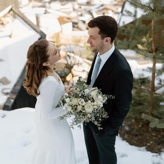 Bride and groom with a white flower bouquet in the snow in front of an Amus Chalet.