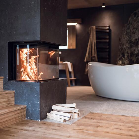 Freistehende Badewanne an einer Felswand mit brennendem Kamin im Vordergrund.