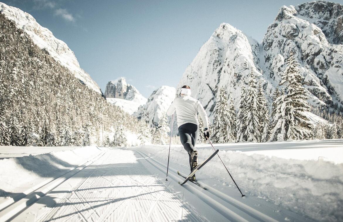 Fondista in un paesaggio innevato tra boschi e montagne, con le Tre Cime di Lavaredo sullo sfondo.