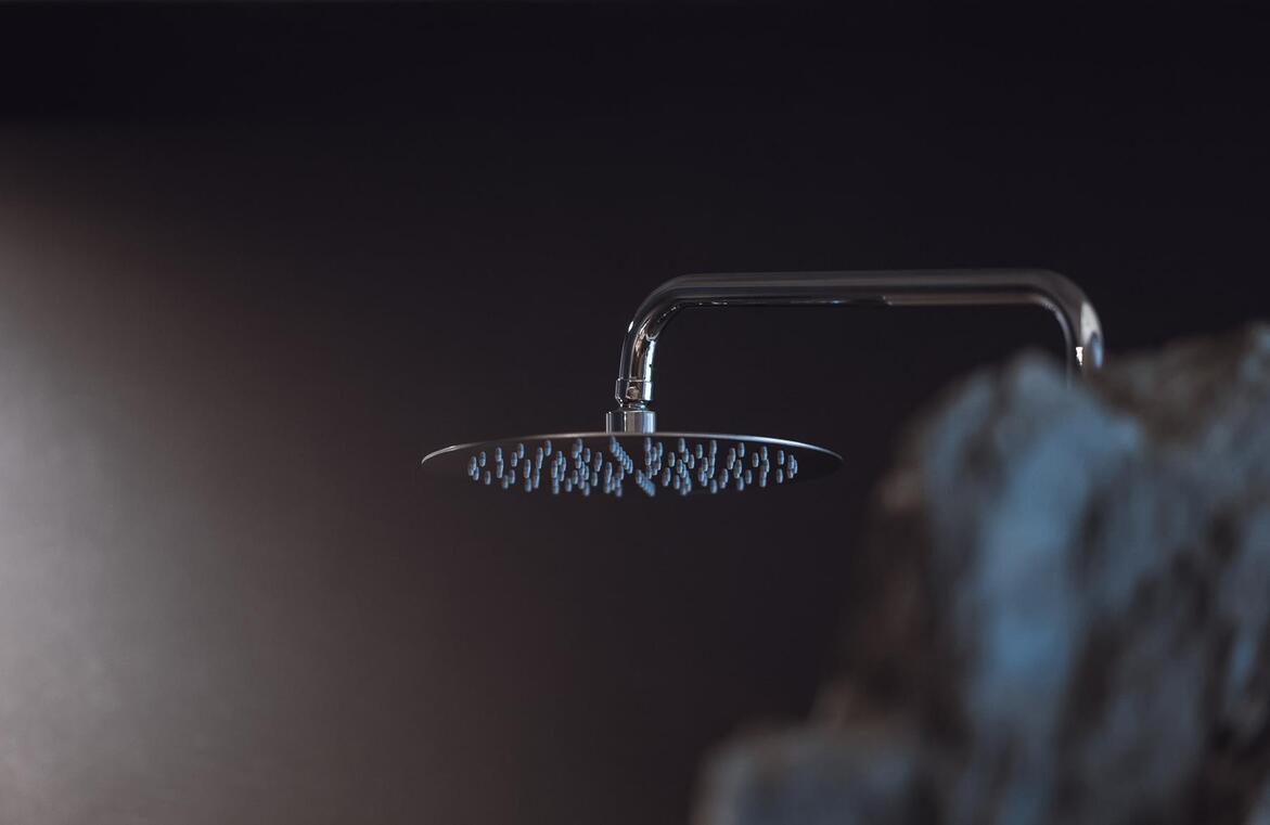 Detailansicht einer Regendusche an einer Felswand mit dunkeln Fliesen im Hintergrund.