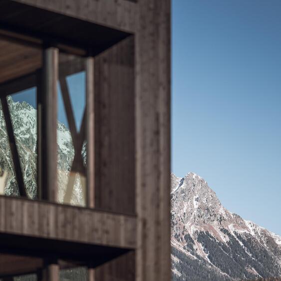 Dark wooden façade of a chalet with towering mountains in the background.