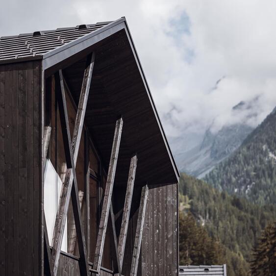 Amus Chalet in dark wood with diagonal wooden elements, large glass fronts and mist-shrouded mountains in the background.