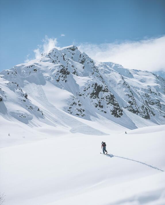 Snowshoe hiker in a vast snowy landscape, with mountains in the background.