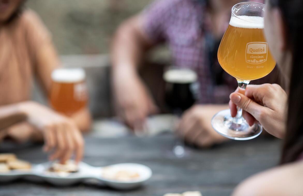 Several people sitting at a table, with a woman holding a glass of beer in the foreground.
