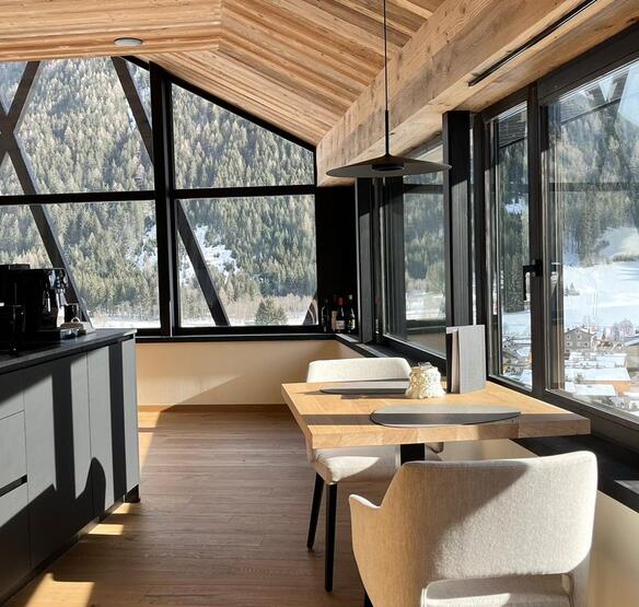 Luminosa zona pranzo degli Amus Chalets con angolo cottura, tavolo in legno e ampie finestre panoramiche.